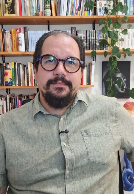 Dr. Leandro Groba, psicanalista, em seu consultório com estante de livros ao fundo